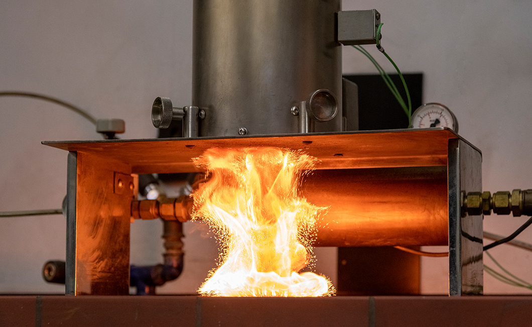 Paper des Monats 12/2020: TF Infrastruktur Zur Bestimmung der Mindestzündtemperatur wird ein Staub/Gas/Luft-Gemisch in eine erhitzte Zündapparatur eingeblasen. Eine Flammenausbildung zeigt die erfolgte Zündung