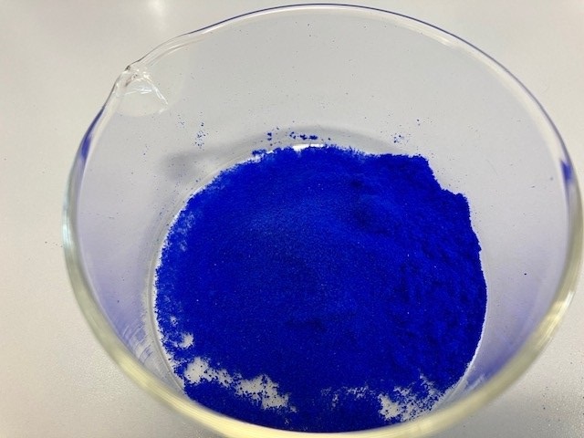 Odysseus Headerbild Ein blaues Pulver in einem Glasgefäß.