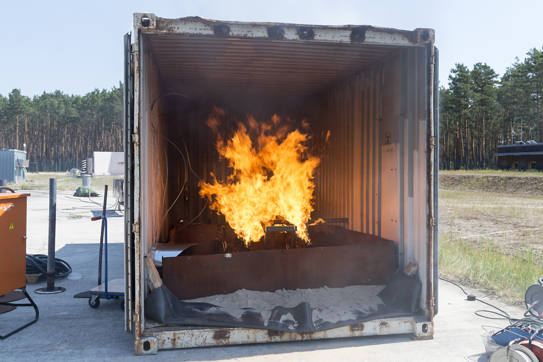 [Translate to English:] Ein Container in freiem Gel&auml;nde, in dem ein Feuer brennt.