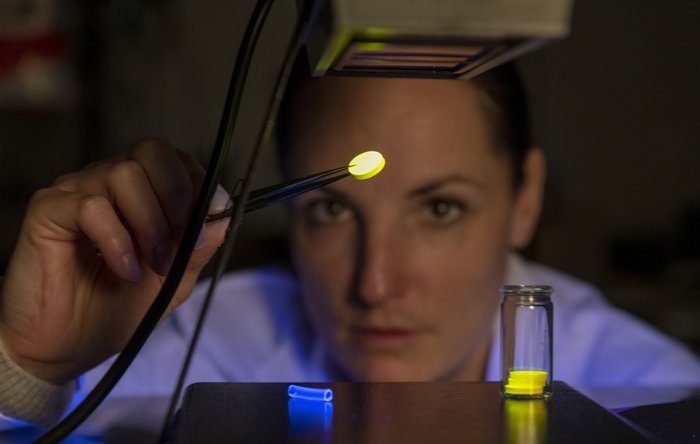 A woman examines materials under fluorescent light.