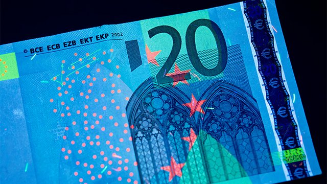 A bank note under UV light with glowing security features. Tile preview