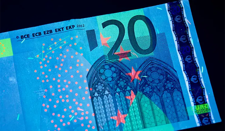 A bank note under UV light with glowing security features.