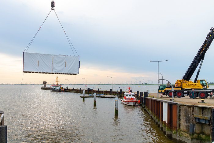 Ein Kran positioniert den Container, der das Meerwasserlabor behausen wird, am Ufer des Eidersperrwerk.