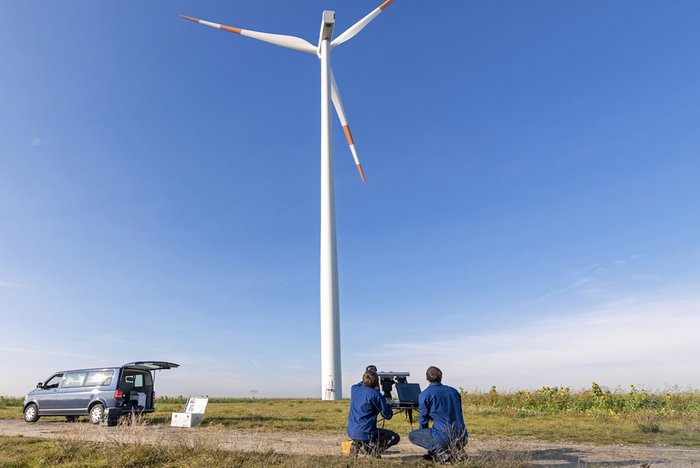 Two scientists with technical equipment in front of a wind turbine in a field