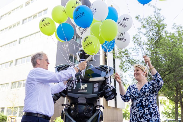 Die Regierende B&uuml;rgermeisterin Franziska Giffey und Prof. Dr. Ulrich Panne &uuml;bernehmen vom Roboter Nox einen Strauss Luftballons.