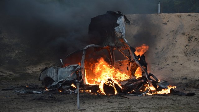 Blick auf das ausbrennende Auto-Wrack Kachel Vorschau