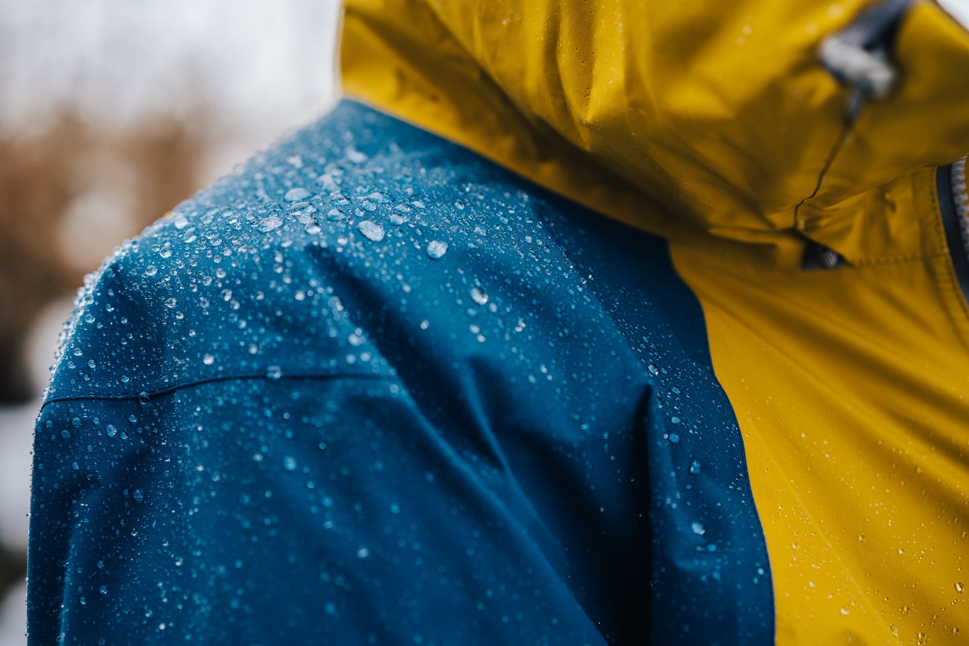 Close-up of a blue-and-yellow outdoor jacket with raindrops rolling off it.