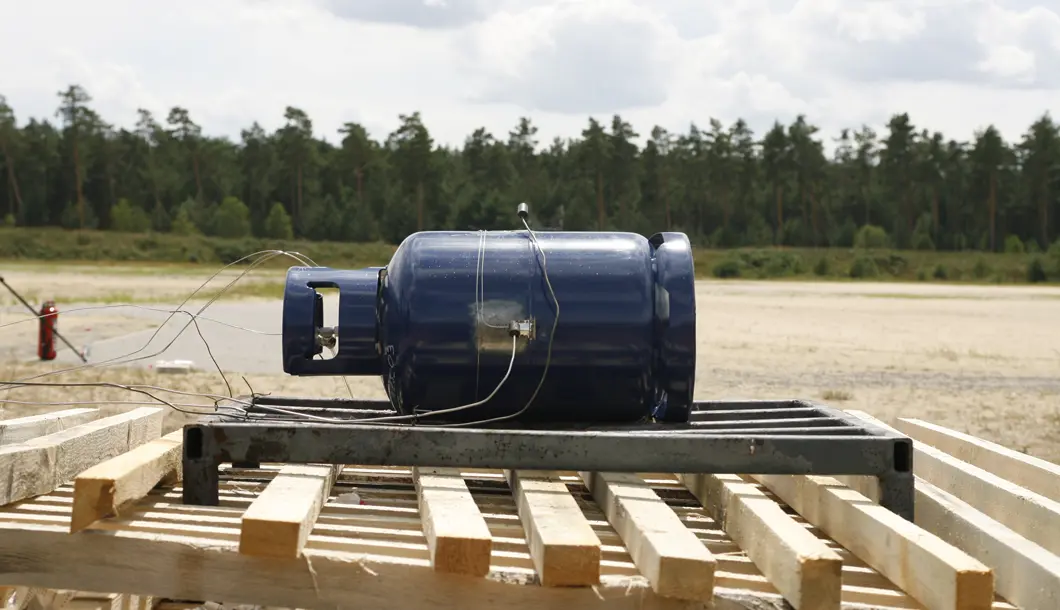 Eine 11 kg Propangasflasche, vorbereitet f&uuml;r einen Unterfeuerungsversuch mit Holz.