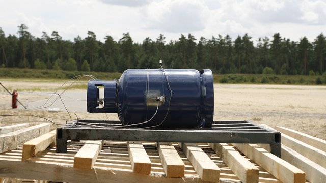 Eine 11 kg Propangasflasche, vorbereitet f&uuml;r einen Unterfeuerungsversuch mit Holz. Kachel Vorschau