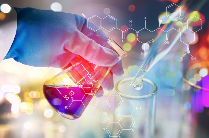 Hände mit Handschuhen halten ein Laborglas, das eine Flüssigkeit enthält. Eine Flüssigkeit wird mit einer Pipette in ein Laborglas getropft.