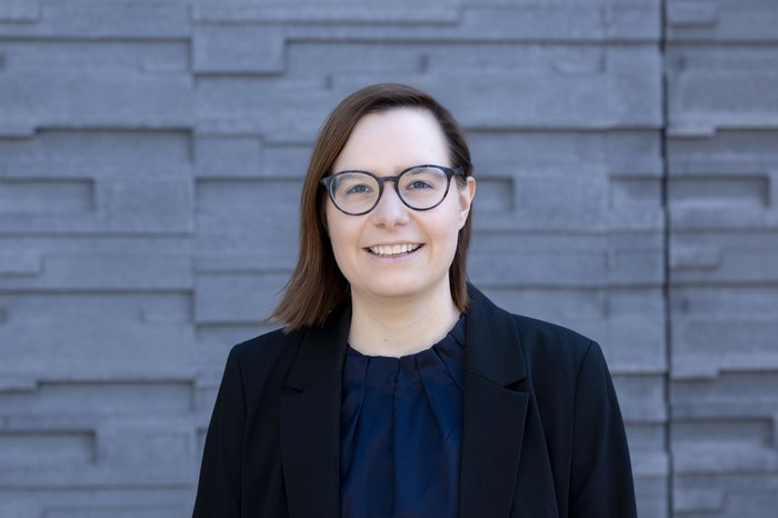 Wissenschaftslerin Janine George vor grauem Hintergrund in schwarzem Blazer, schwarz umrandeter Brille